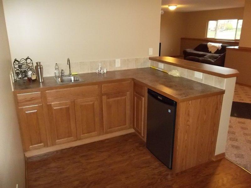 With oak cabinets and laminate countertop. Bar refrigerator under cabinet and tile backsplash.